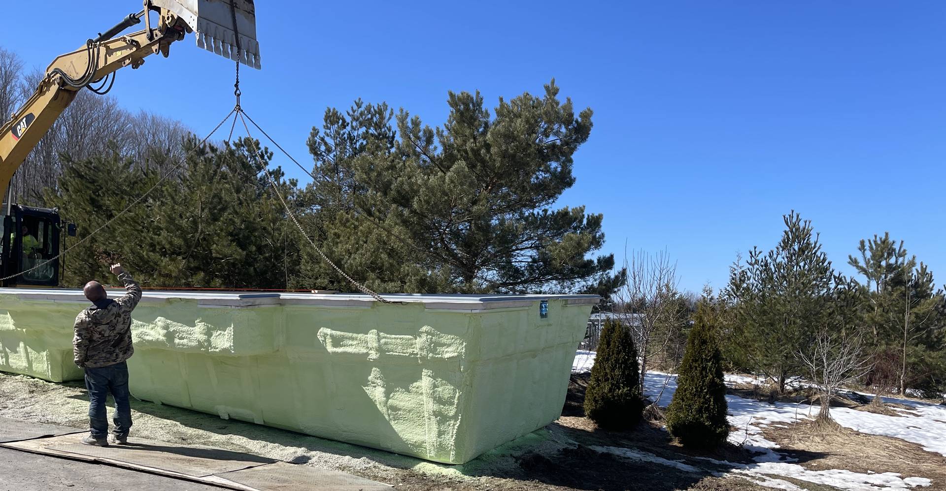 A large green dumpster sitting next to trees.